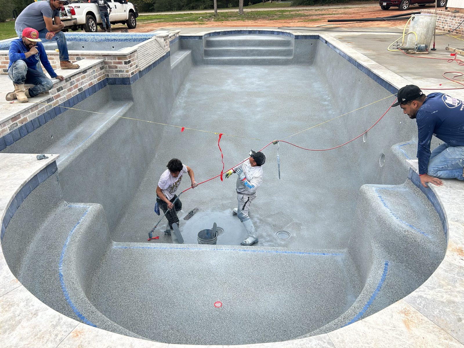 Crew hand-troweling fresh interior finish inside an empty pool shell with tile band and brick spa wall